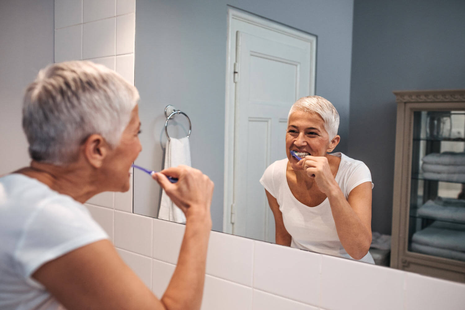 Woman with short white hair sticks to her oral hygiene routine and brushes her teeth