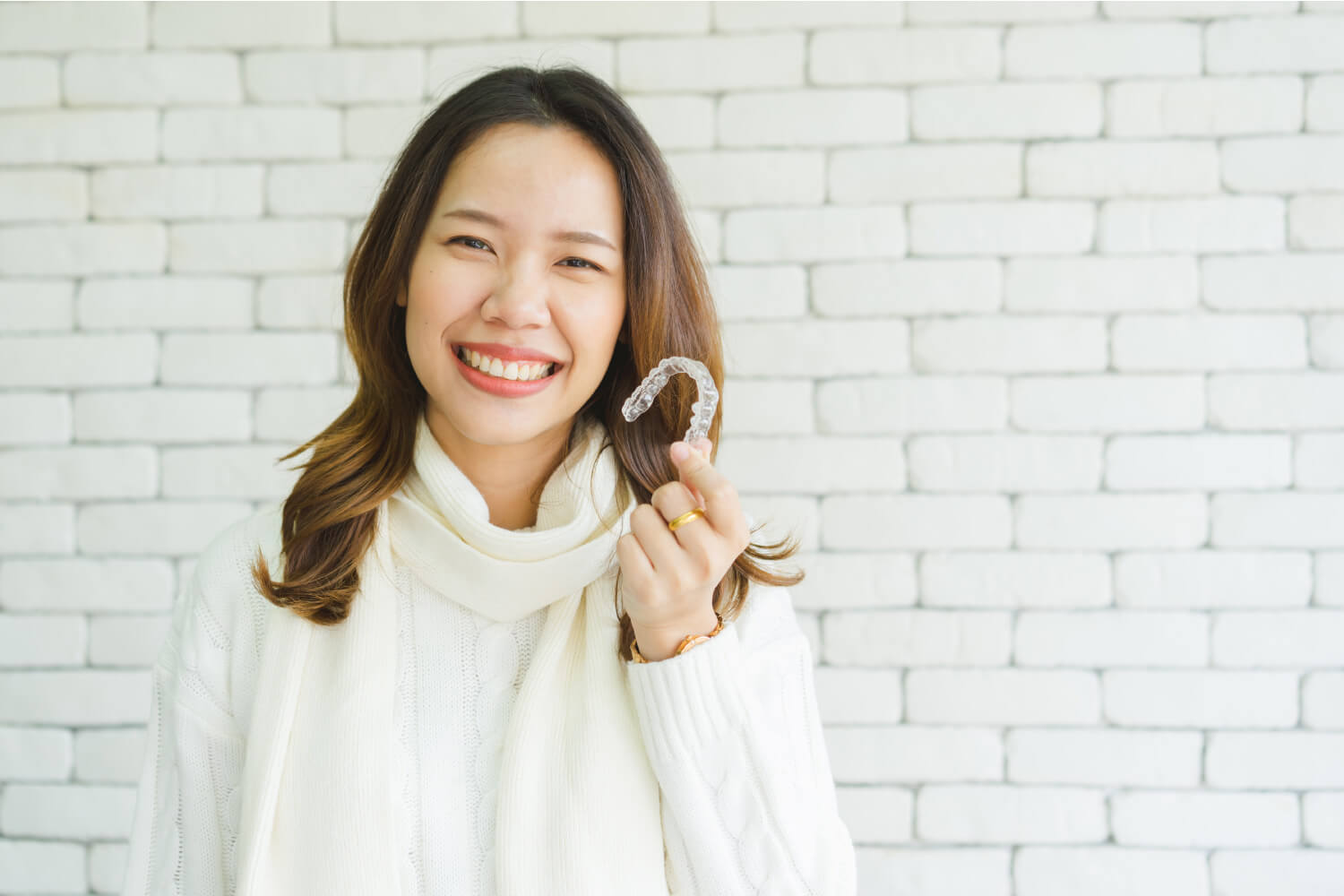 Adult woman smiles as she holds up Invisalign clear aligners in Wolcott, Ct