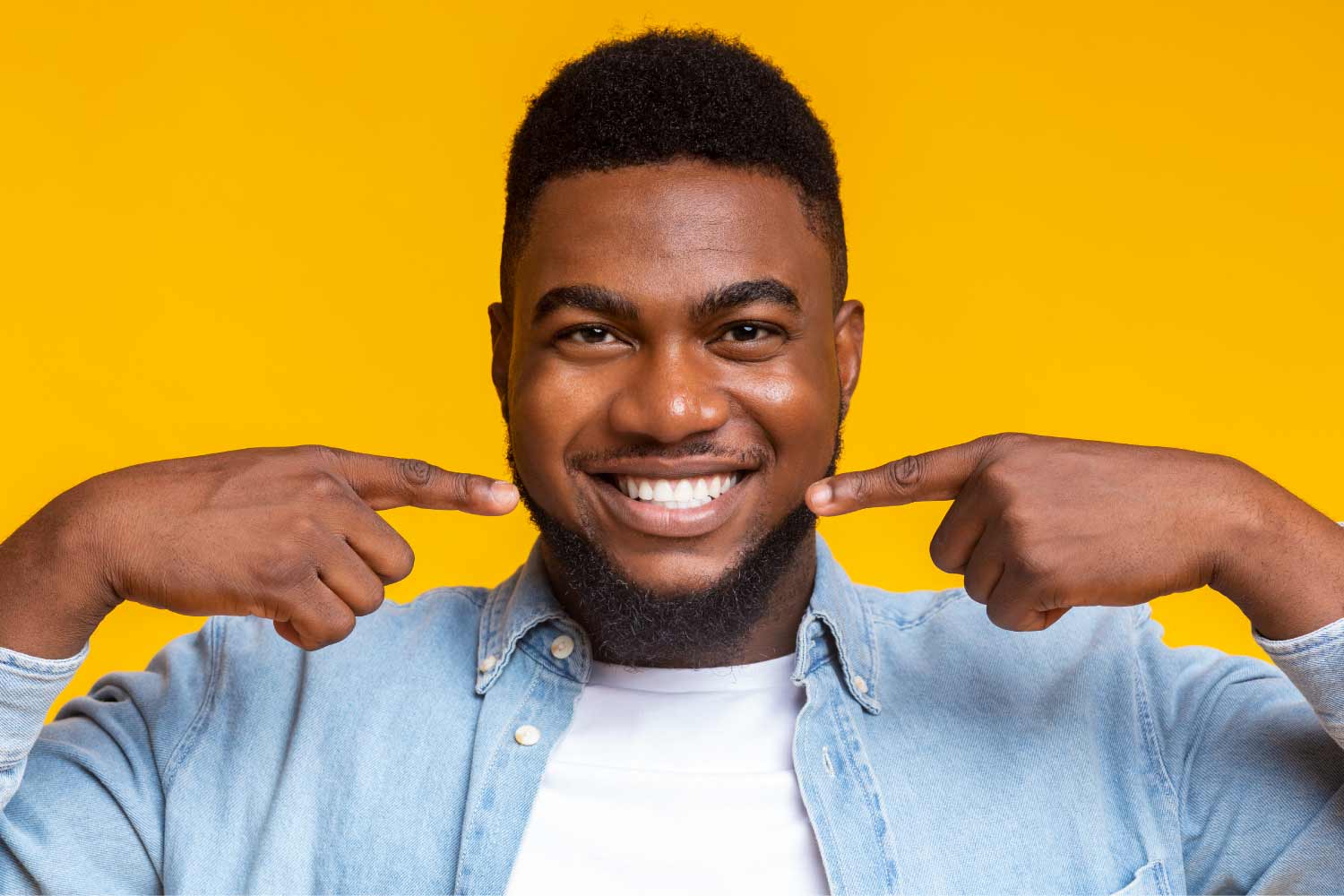 Dark-haired man smiles and points to his teeth after teeth whitening