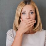 Blonde woman covers her mouth in embarrassment due to gum disease causing receding gums