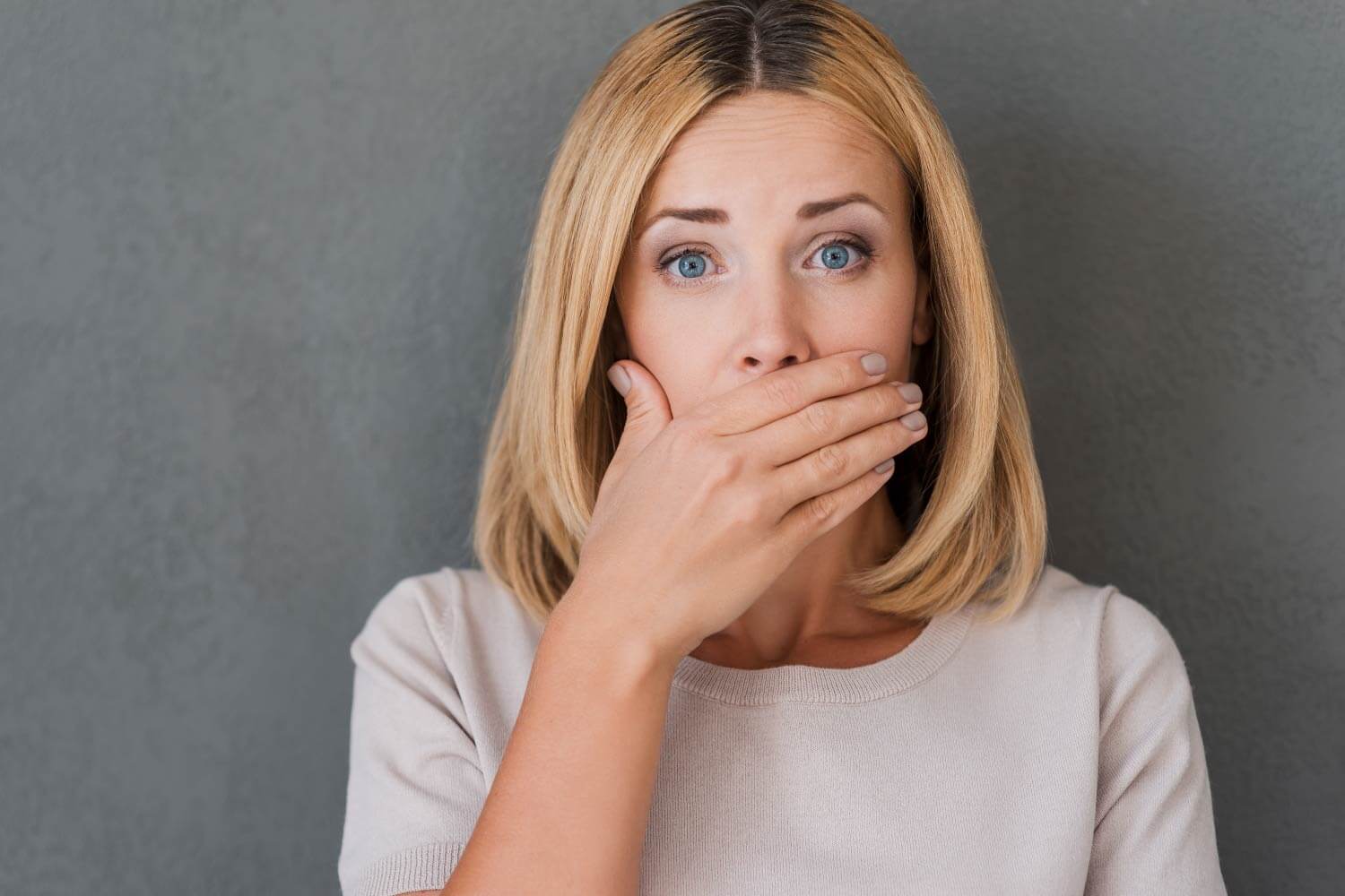 Blonde woman covers her mouth in embarrassment due to gum disease causing receding gums