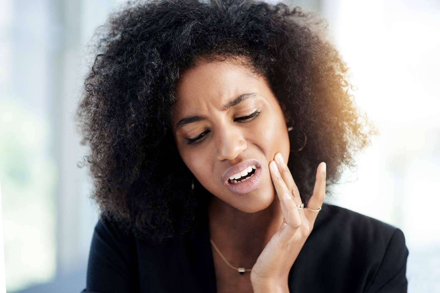 A curly haired woman cringes in pain because she needs root canal therapy