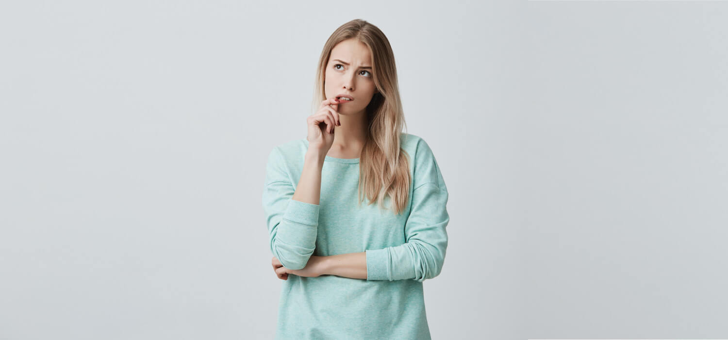 Blonde woman in a turquoise shirt touches her lip as she wonders if she has a tooth stain vs. cavity