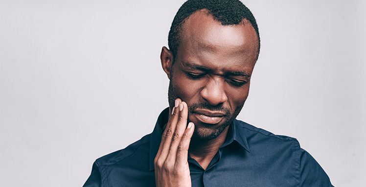 man grimacing and holding right cheek