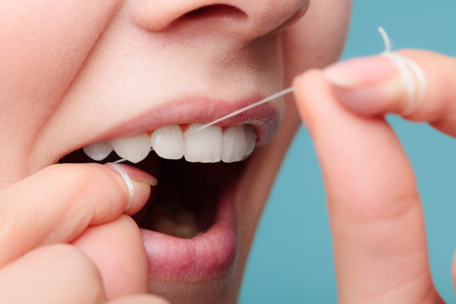Closeup of a woman using string floss to clean between her teeth
