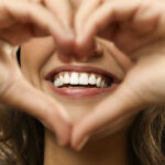 closeup of a brunette woman holding her hands in a heart in front of her smile
