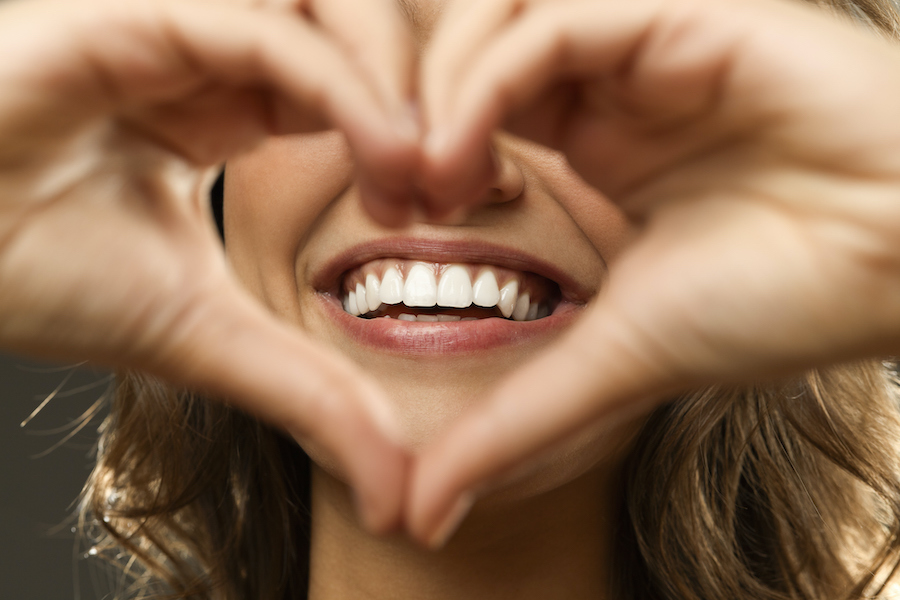 closeup of a brunette woman holding her hands in a heart in front of her smile